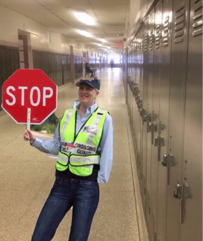 Ms. Laughingstock holds a stop sign to regulate traffic in the third floor hallway.